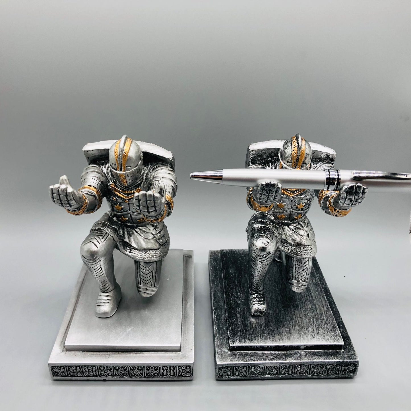 Metallic knight figurines with pen holders on a gray background