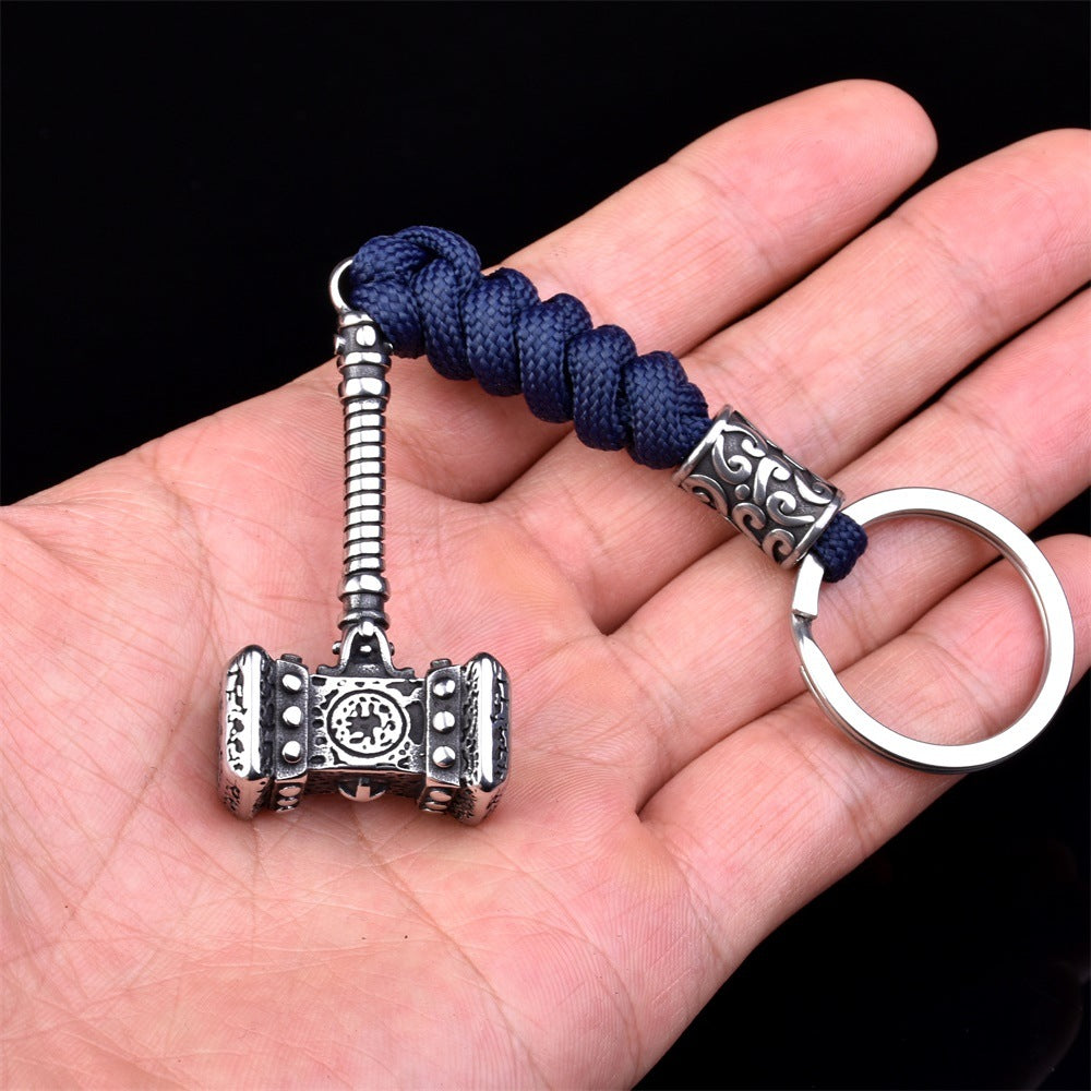 Silver Mjällnir keychain with blue cord held in a hand against a black background