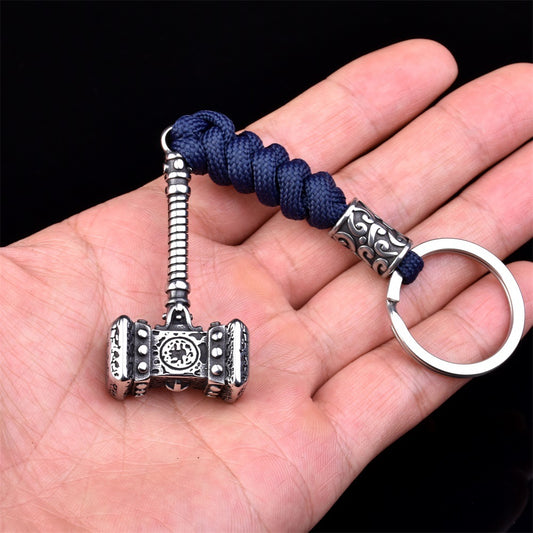 Silver Mjällnir keychain with blue cord held in a hand against a black background